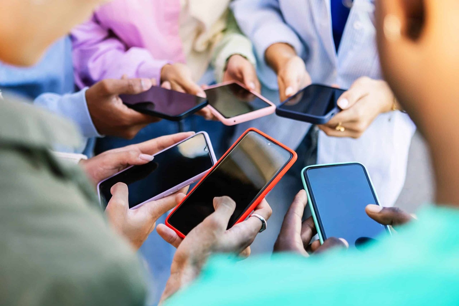 Photo: Young group of people standing in a circle using a cellphone outside.